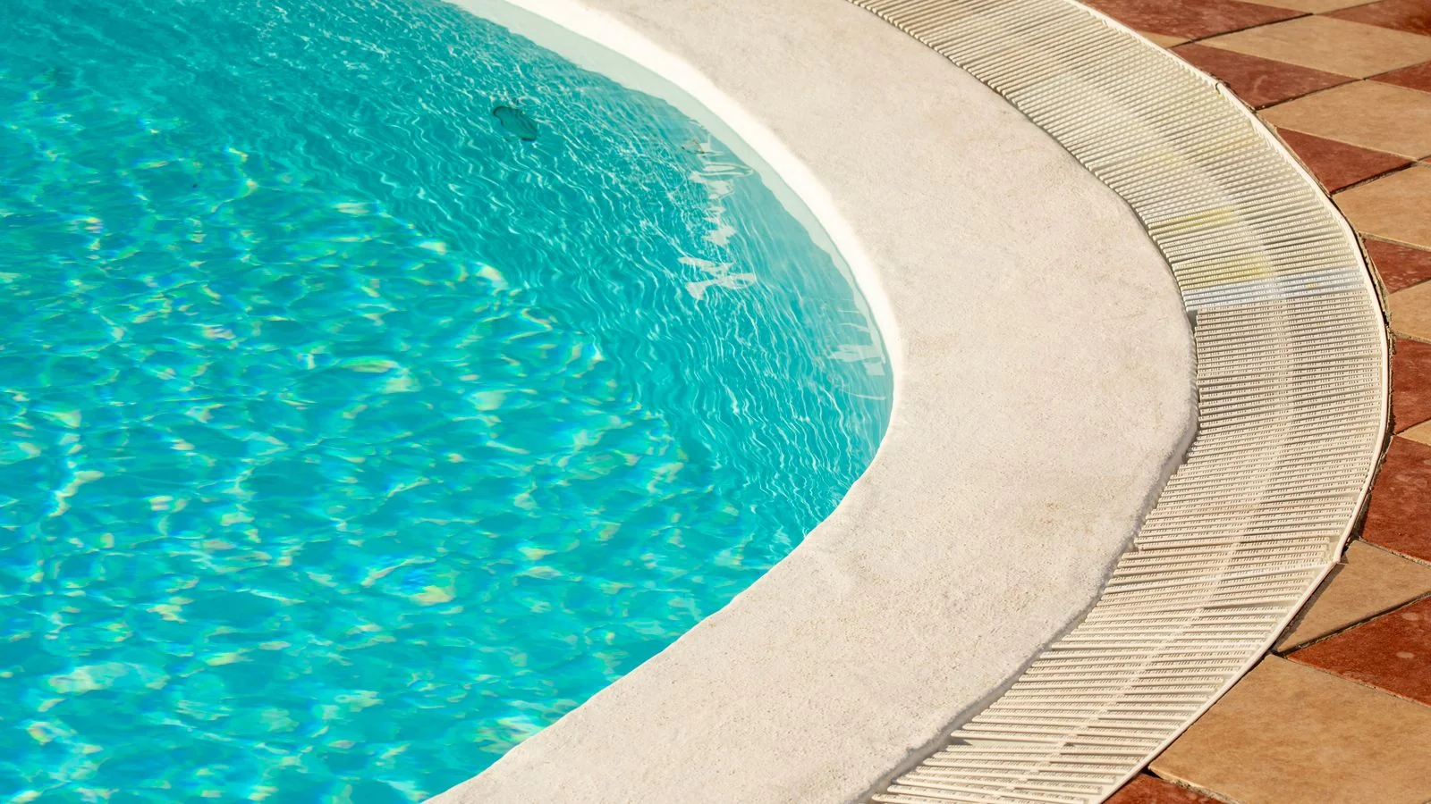 A tranquil, sunlit luxury poolside with clear water and elegant tile edging.