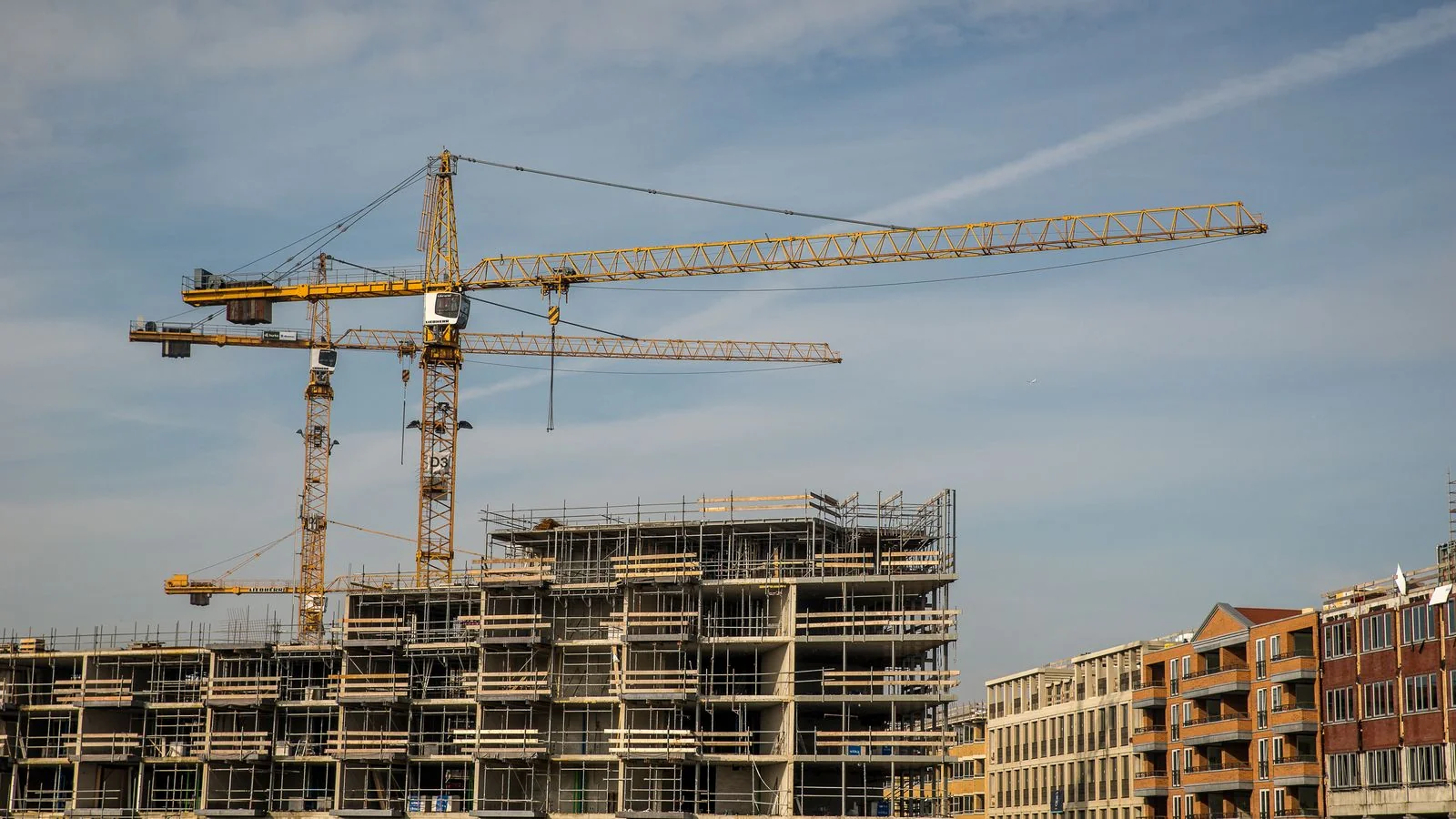 A city construction site with cranes and partially built structures, the stage where neighbors and subcontractors start writing the record.