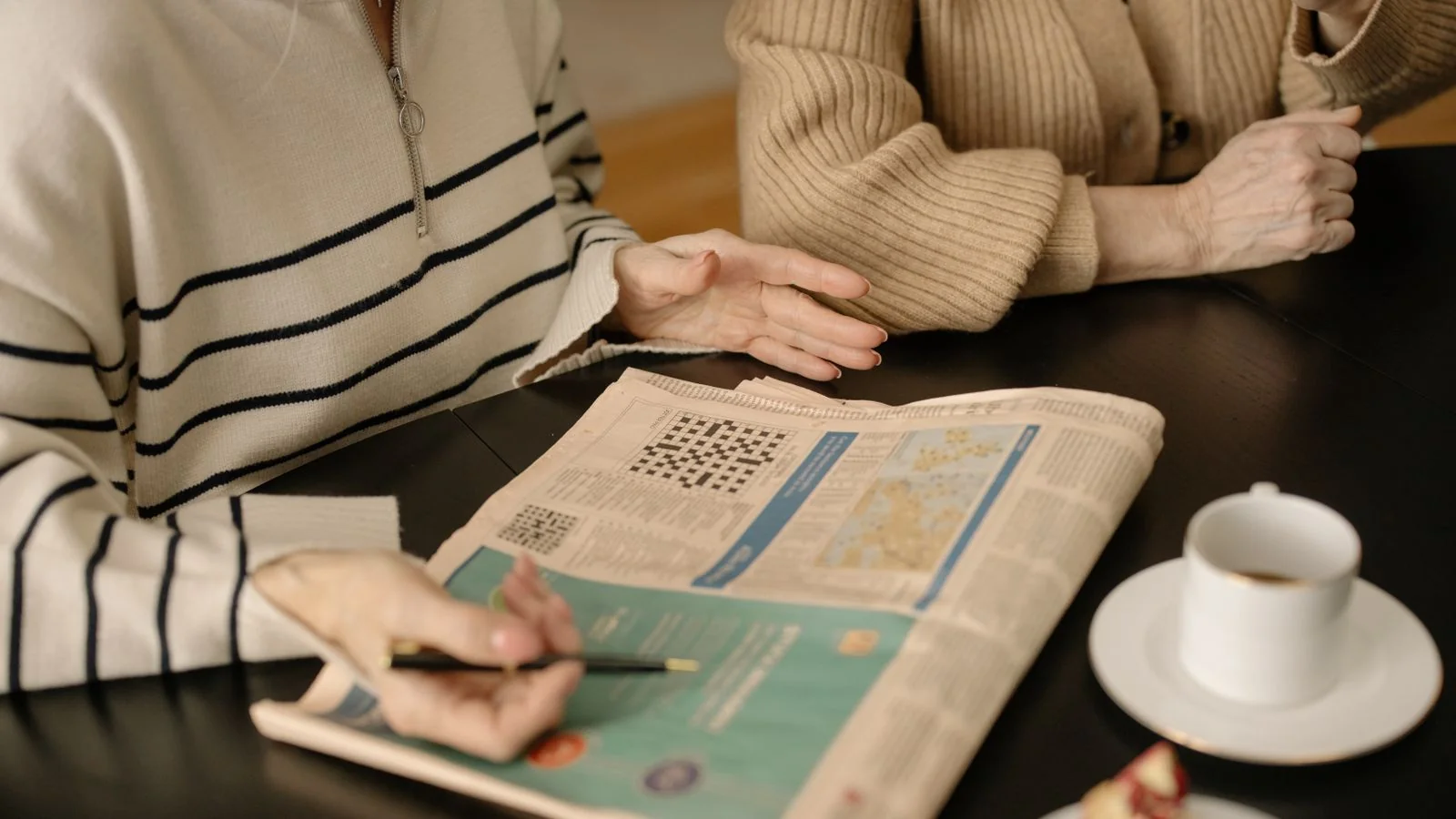 Two older women reading a newspaper together over coffee, the kind of reader a retirement announcement reaches