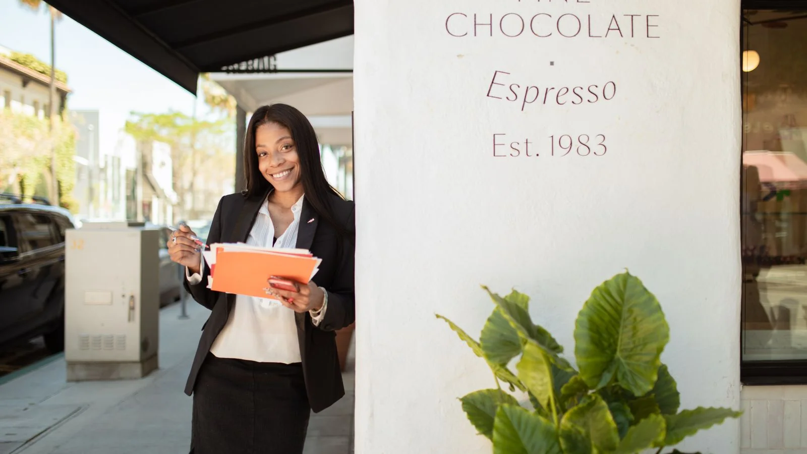 Businesswoman smiling outside a cafe holding documents on opening day