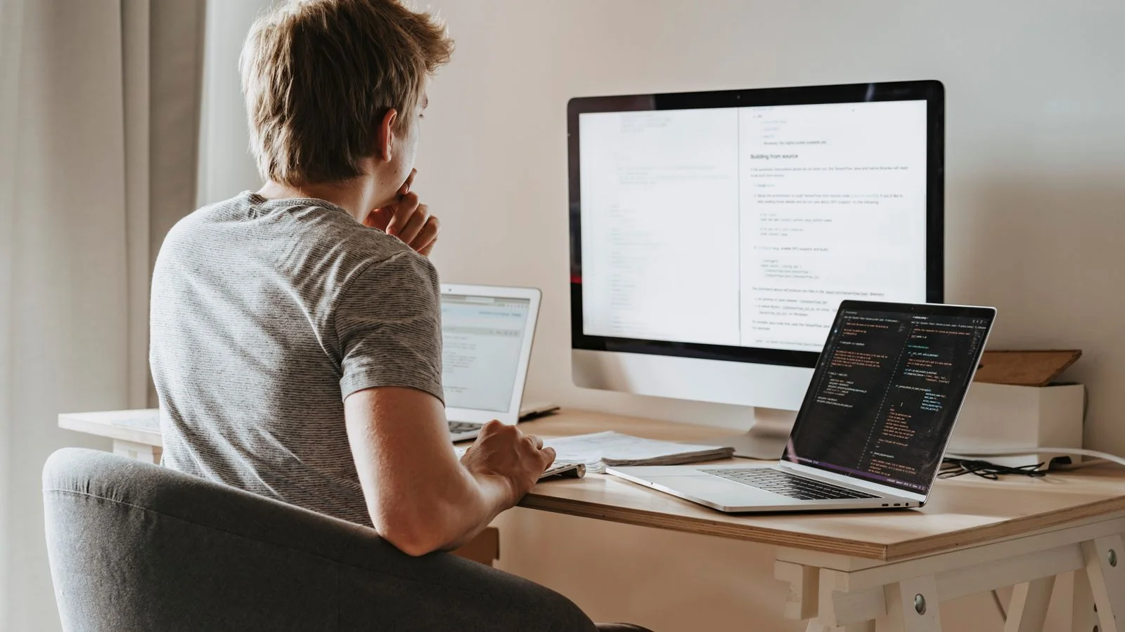 Man works across two laptops and a desktop monitor, comparing profile pages for consistency