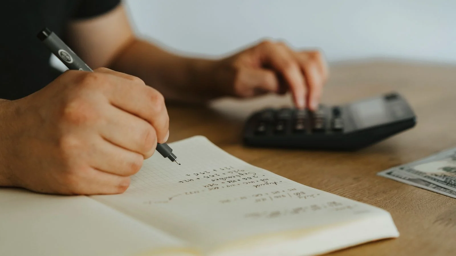 Hands writing calculations in a notebook beside a calculator, the royalty math every indie author runs