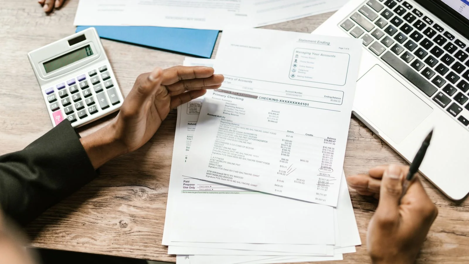 Hands holding financial documents next to a calculator and laptop during a budget review