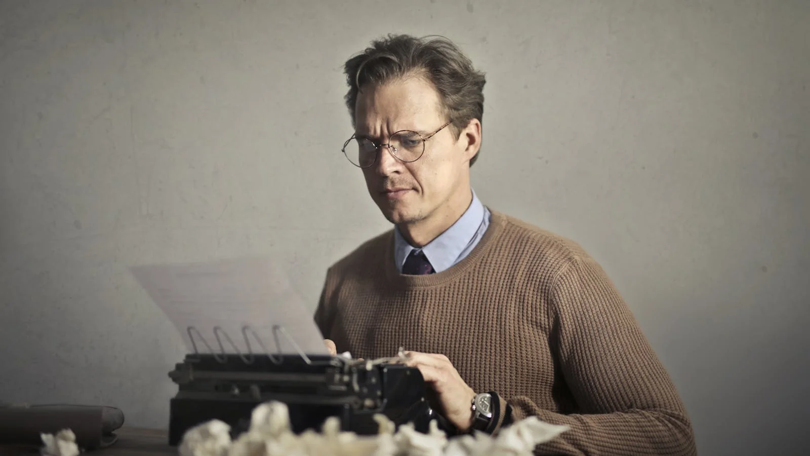 A pensive man typing on a vintage typewriter at a desk, an image used to describe the editorial process every published press release passes through.
