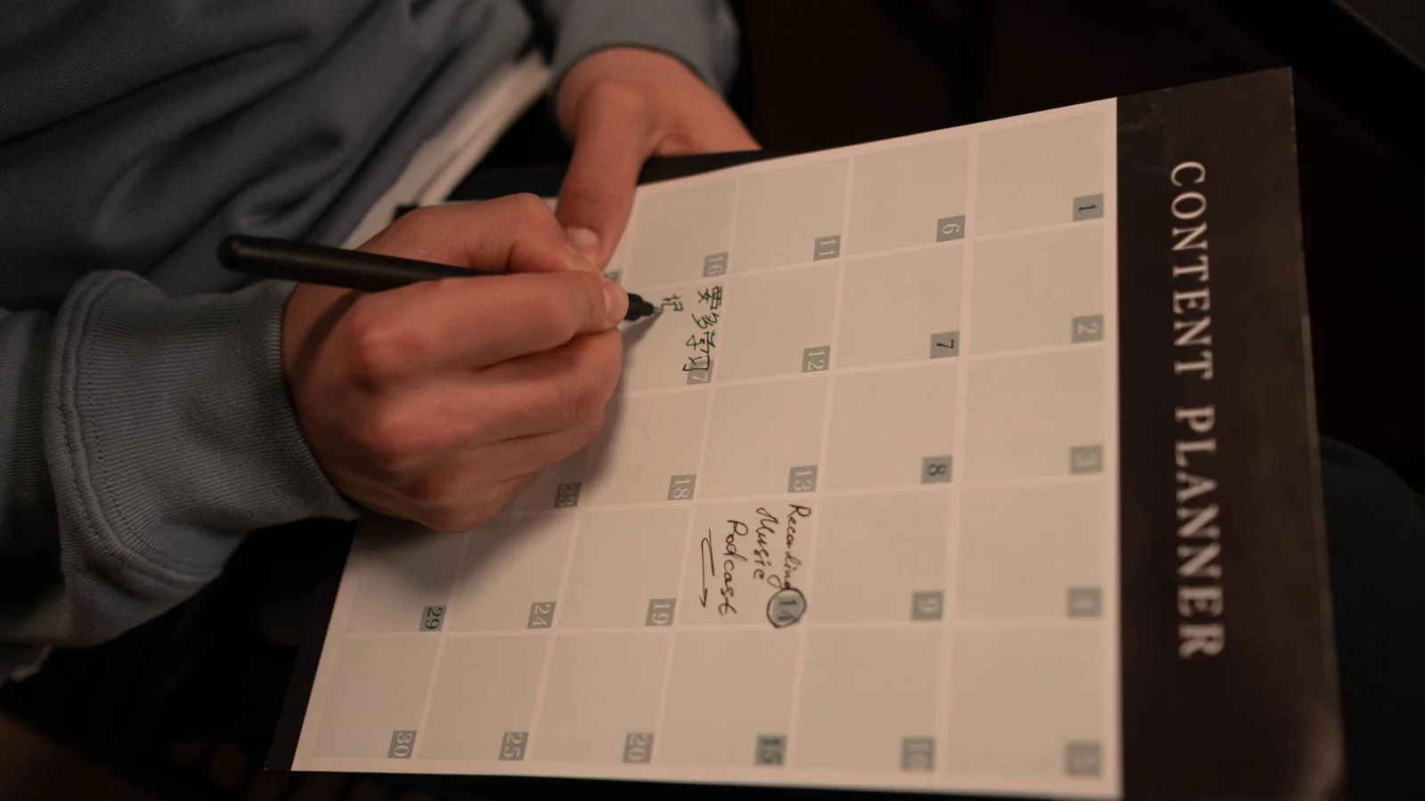 A person writing in a planner at a desk, the deliberate outreach work the technique depends on