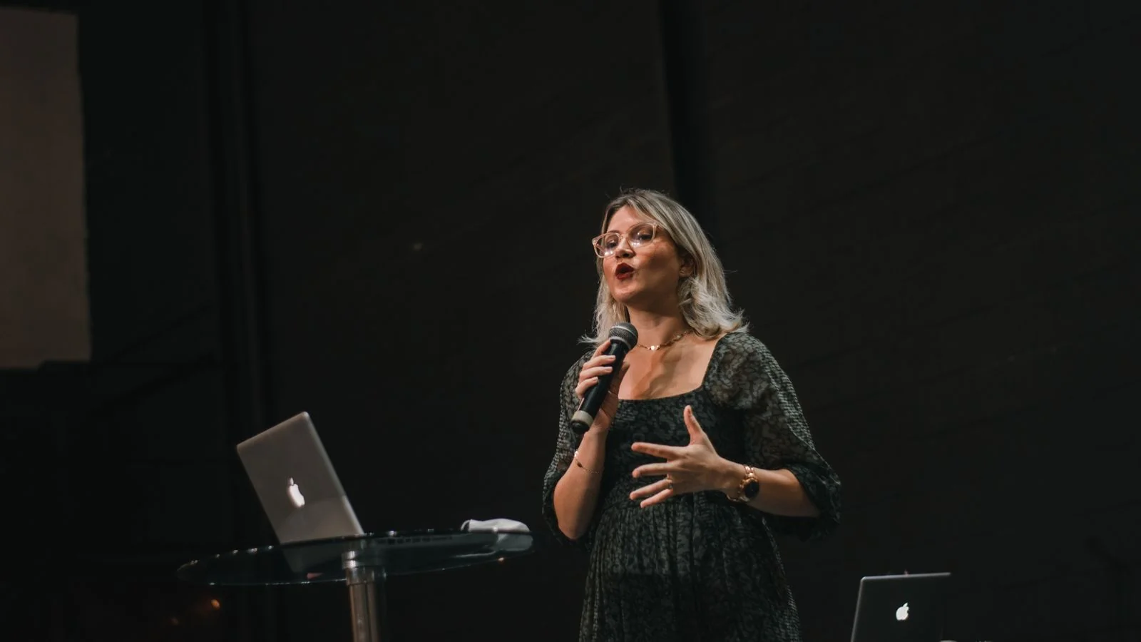 Woman delivering a speech on stage with a microphone and laptop