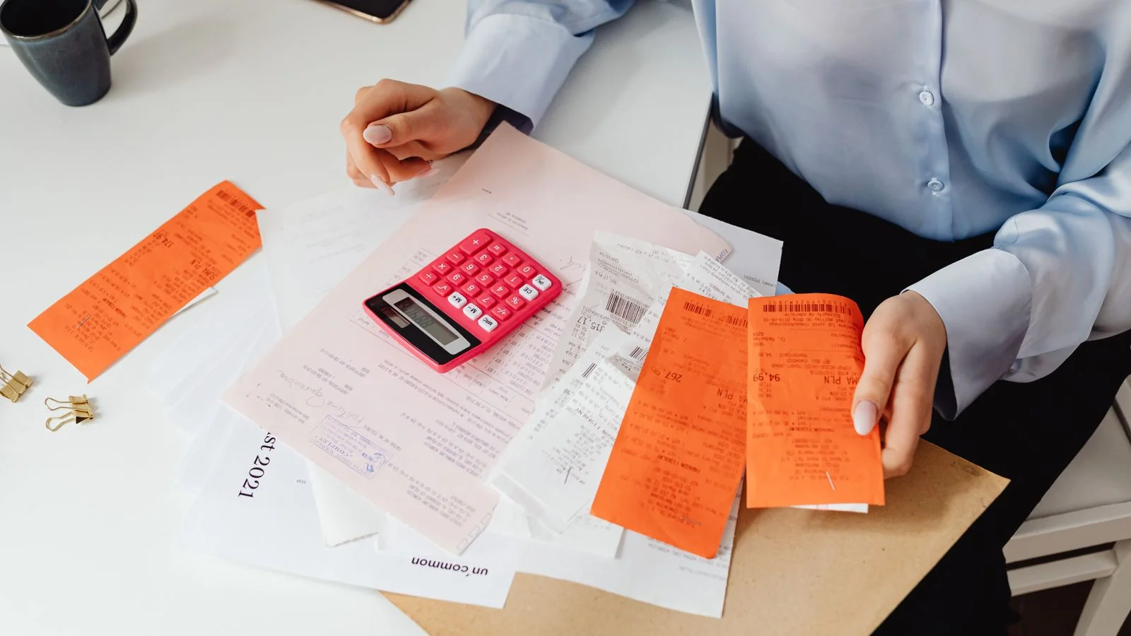 Woman reviewing receipts and adding up expenses on a pink calculator, the math behind platform fees