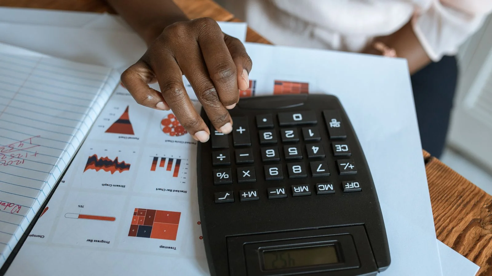 Hand on a calculator over printed financial charts, running newsletter platform fee math