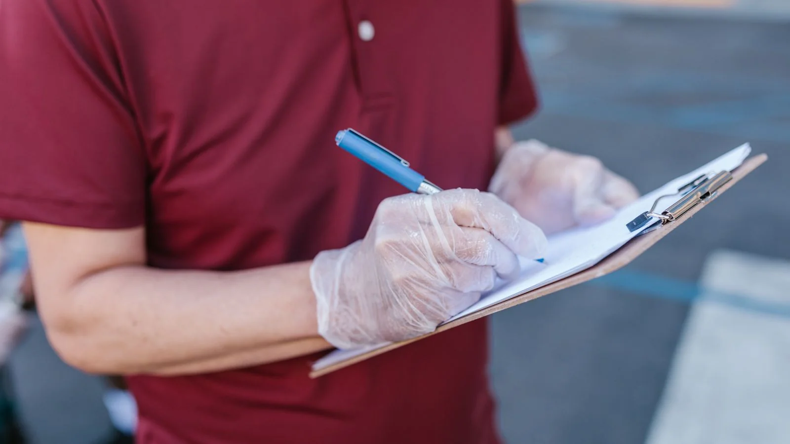Person writing notes on a clipboard while standing outdoors