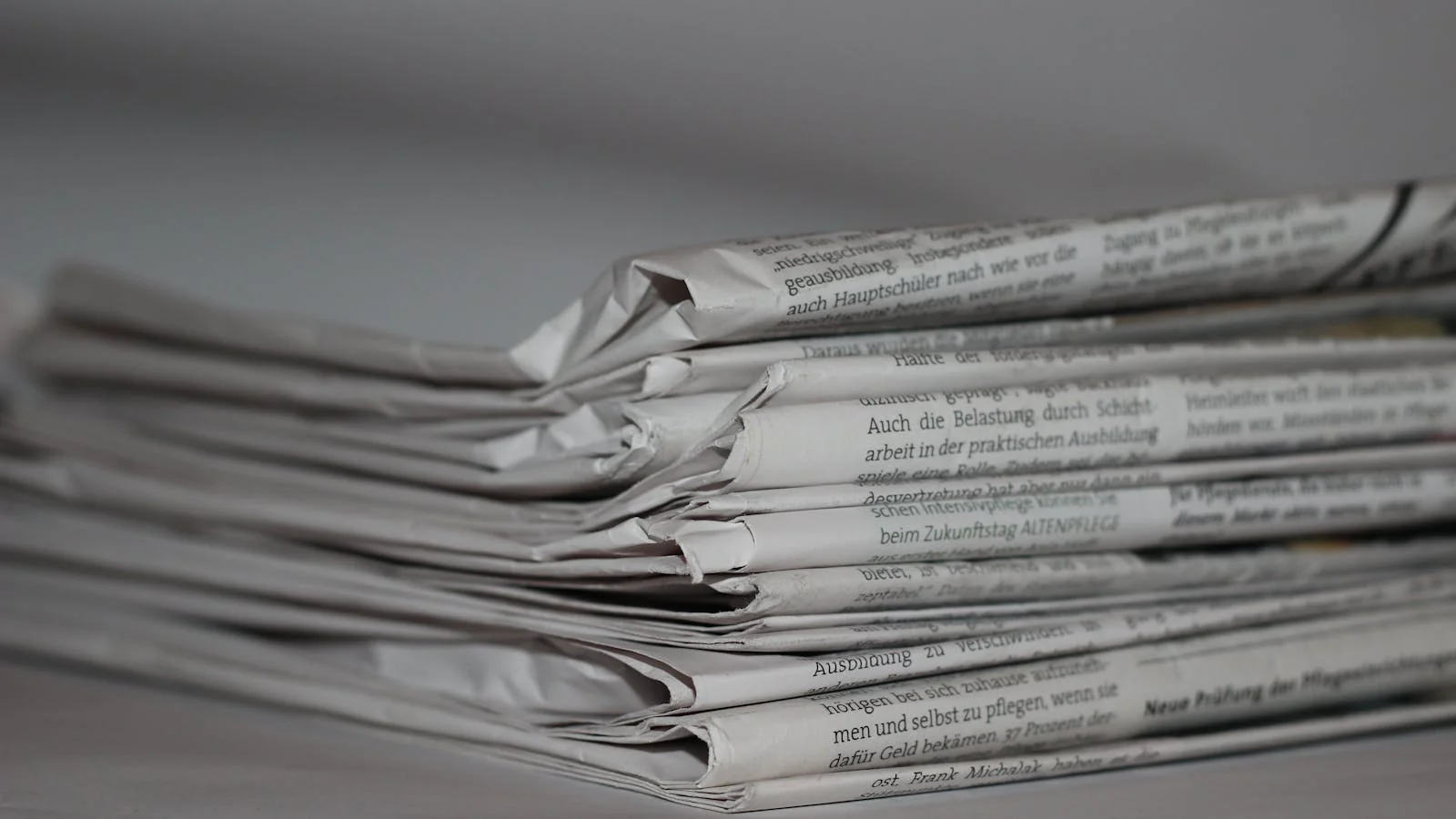 A close-up of folded newspapers stacked on a surface, representing traditional print coverage.
