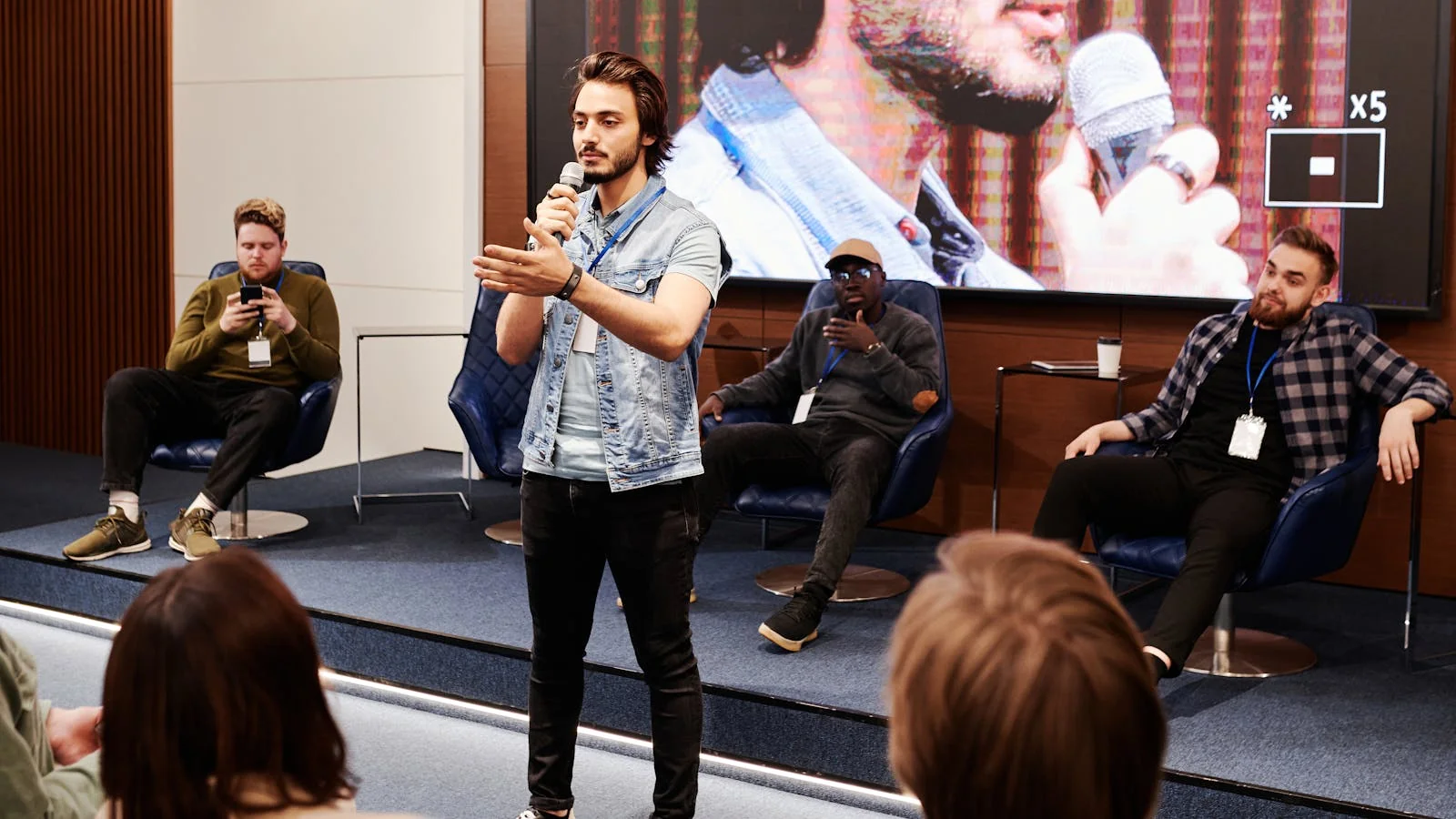 A speaker holding a microphone, mid-point, engaging an audience at an indoor business event