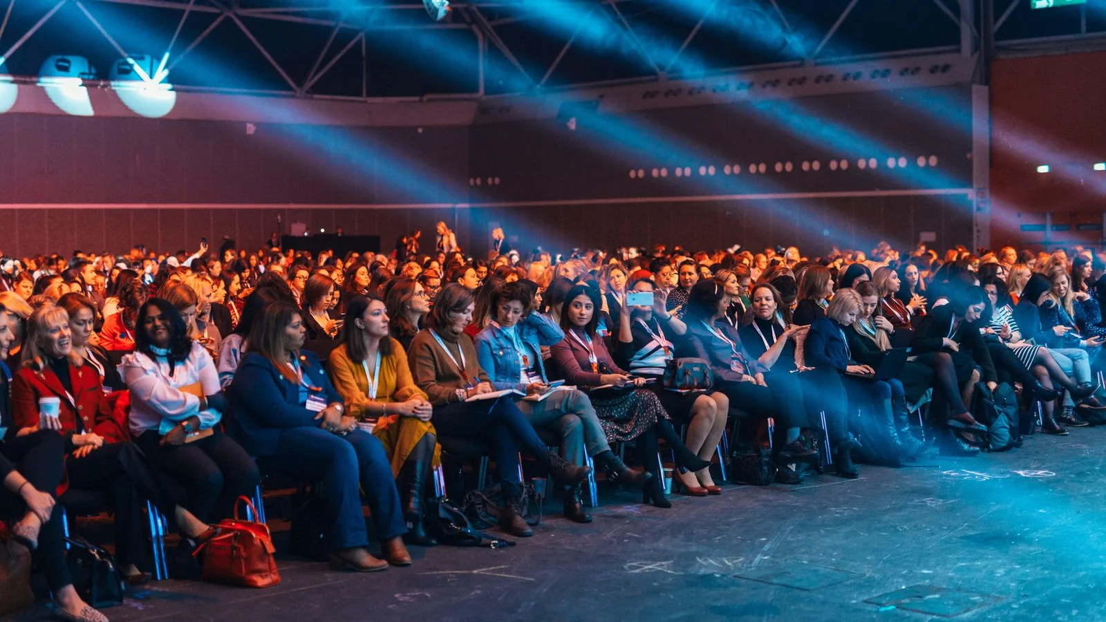 A confident speaker addressing a large seated audience in an auditorium with dramatic lighting