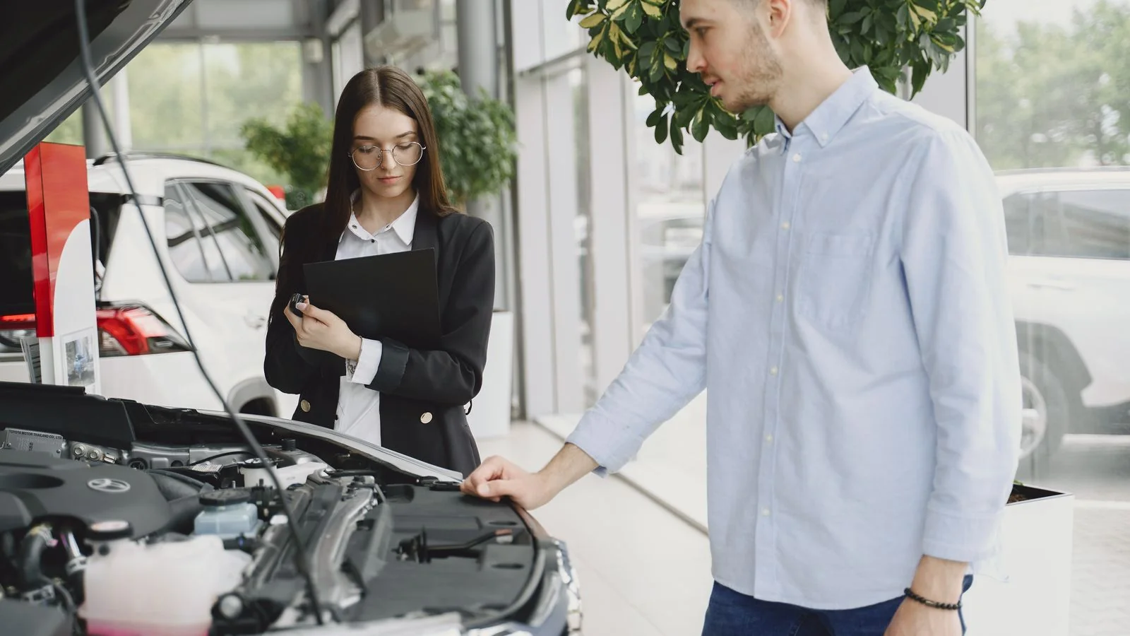 A mechanic and a car owner examining an engine together in a service bay.