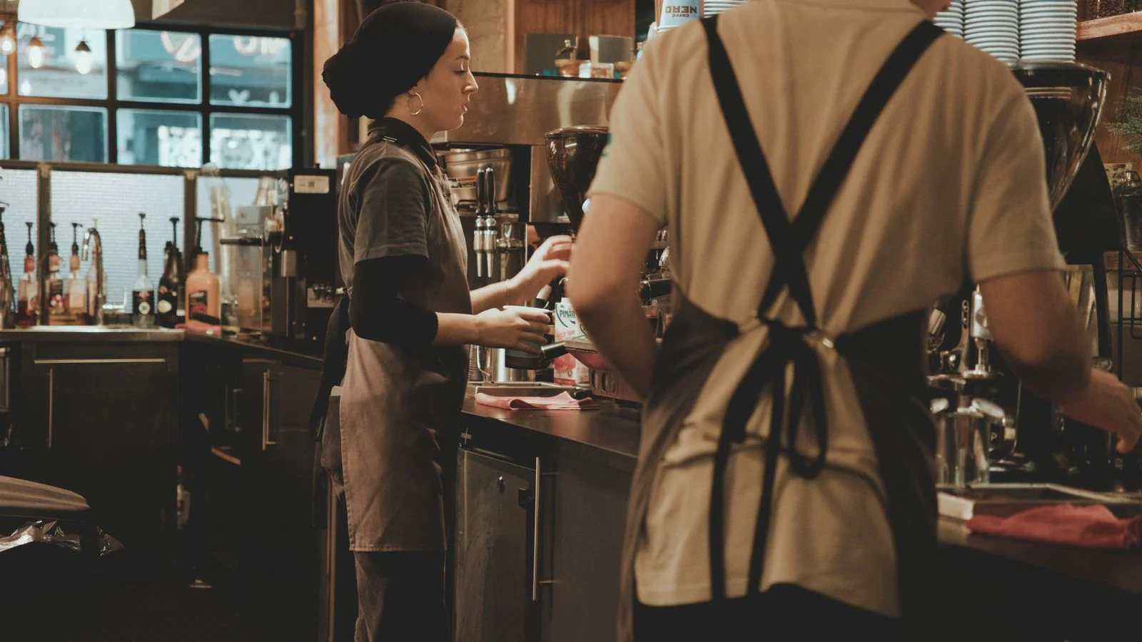 Baristas working behind a busy cafe counter preparing drinks during a morning rush.