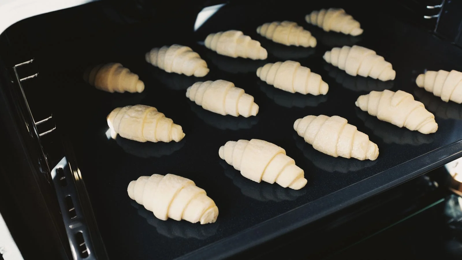 Unbaked croissants arranged on a tray going into the oven in a bakery kitchen.