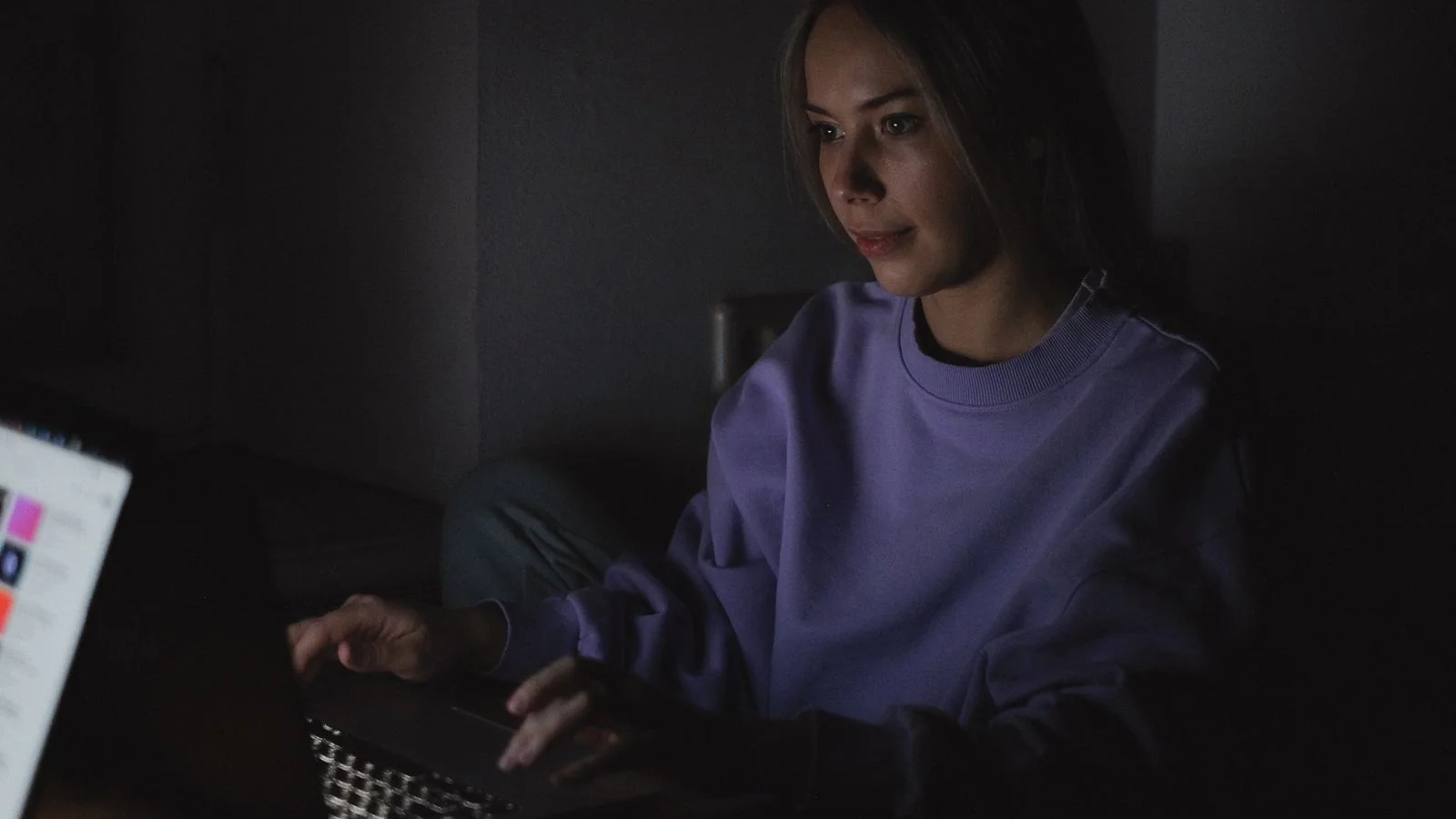 A woman working at a laptop in a dark room, where most positions get written