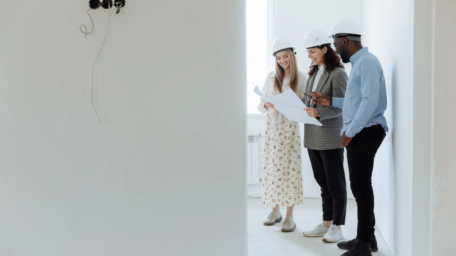 Three professionals in hard hats reviewing building plans inside an unfinished structure, the clients who need the rule explained.