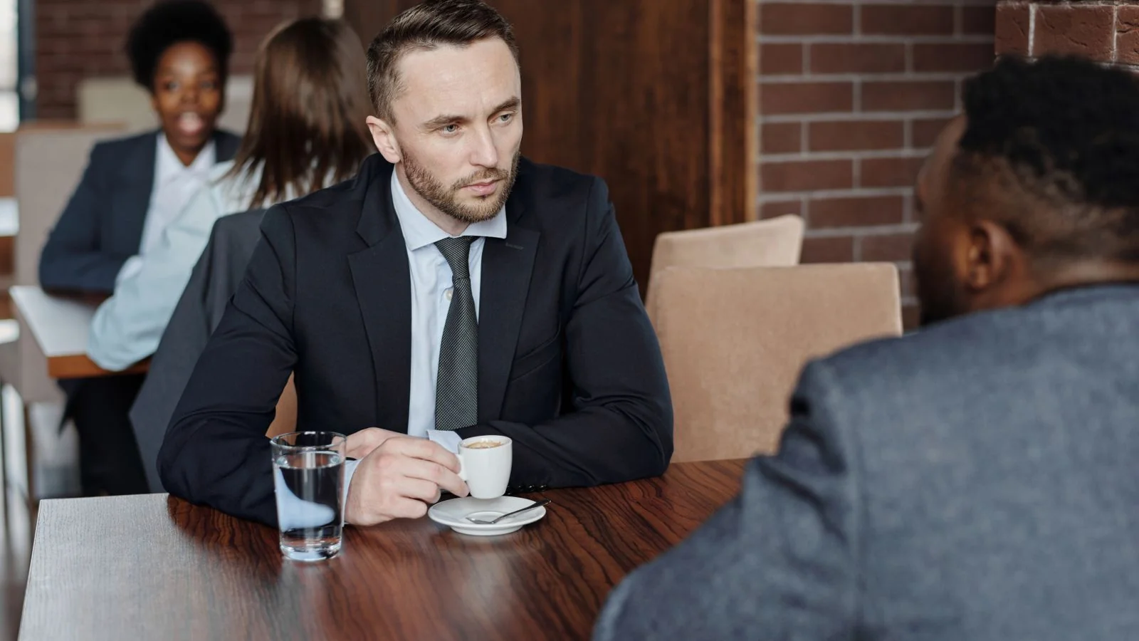 Two people in conversation over coffee, the meeting that follows a reporter finding a local source who publishes real numbers.