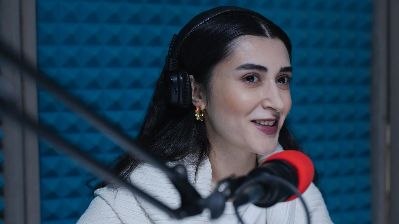 Woman with headphones speaking into a microphone in a podcast studio, one designer saying what she thinks out loud.