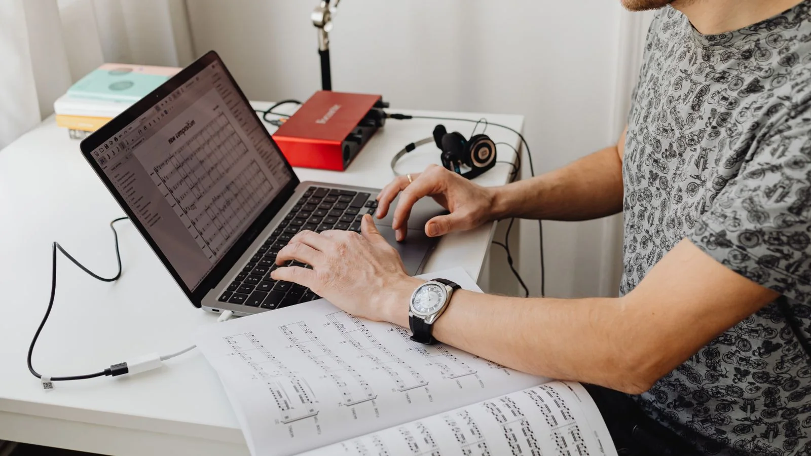 A person writing notes at a desk beside open sheet music