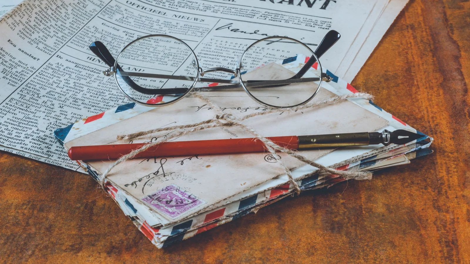 Old letters, a fountain pen, reading glasses and a folded newspaper on a wooden table