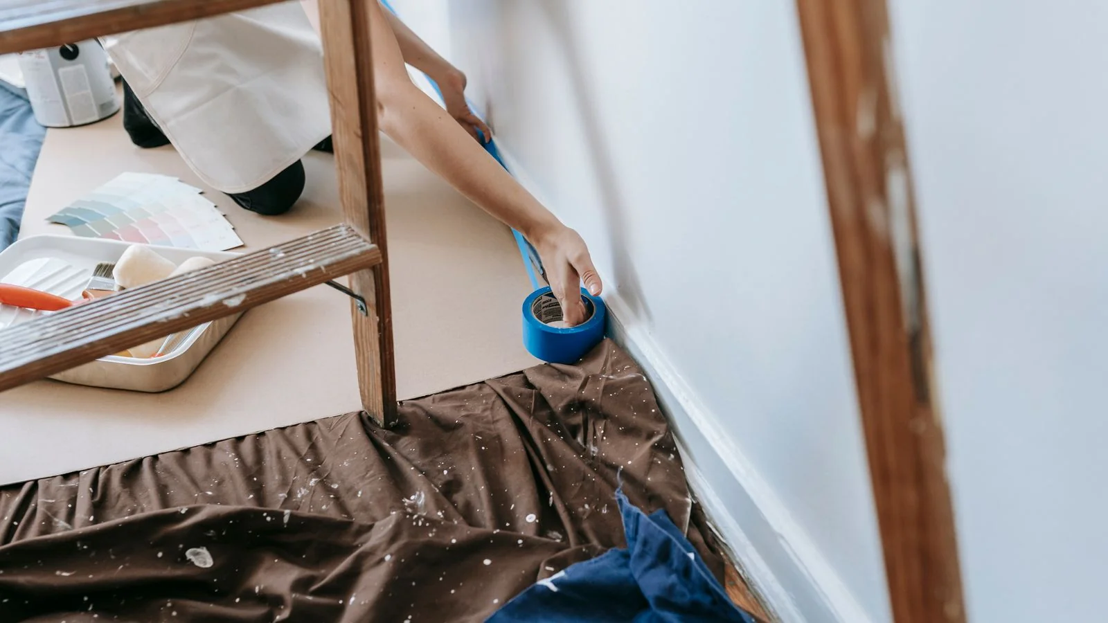 A person carefully applies painter's tape to prepare a wall before painting.