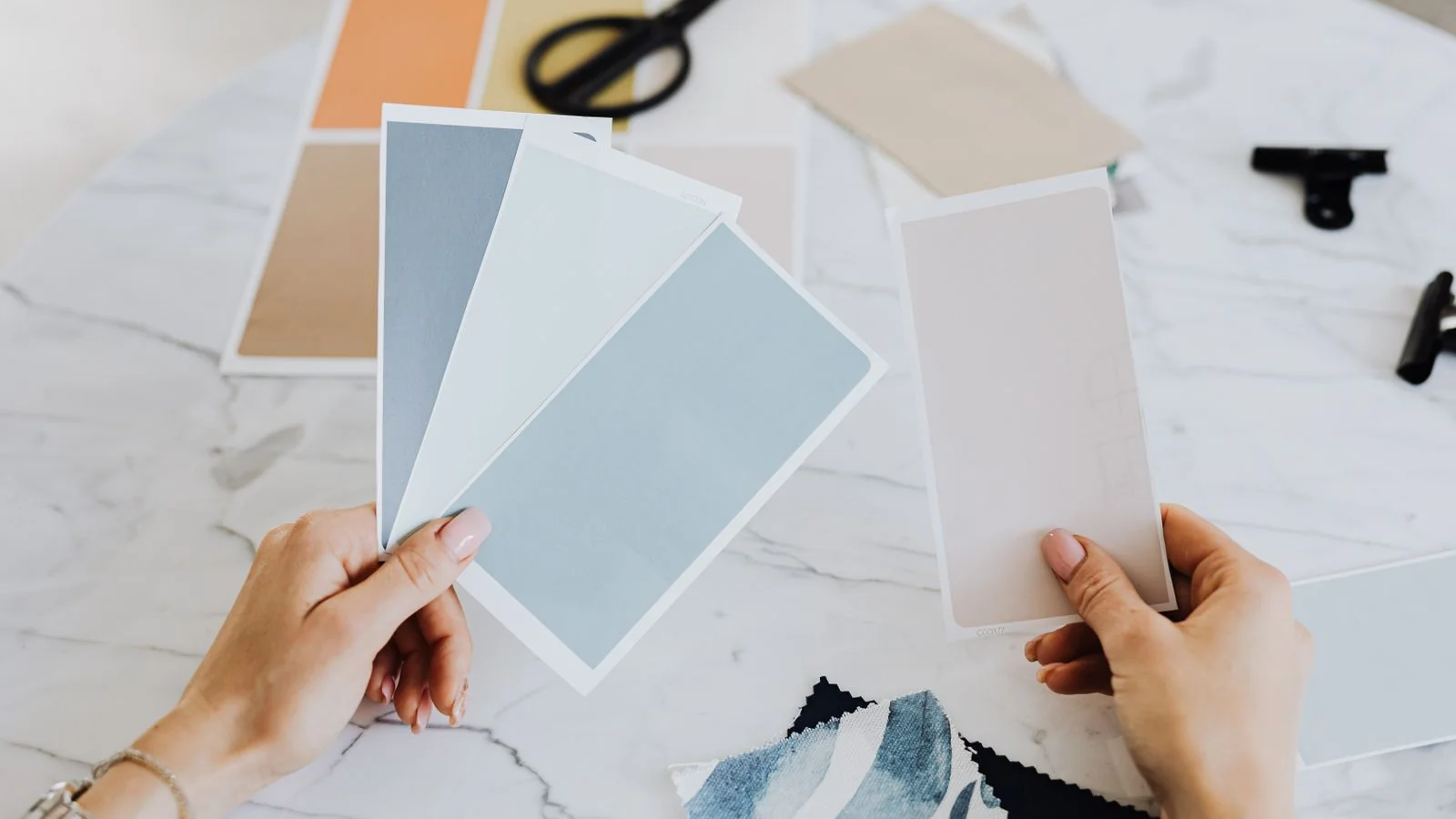 Hands hold a fan of paint color swatches for choosing a room's palette.