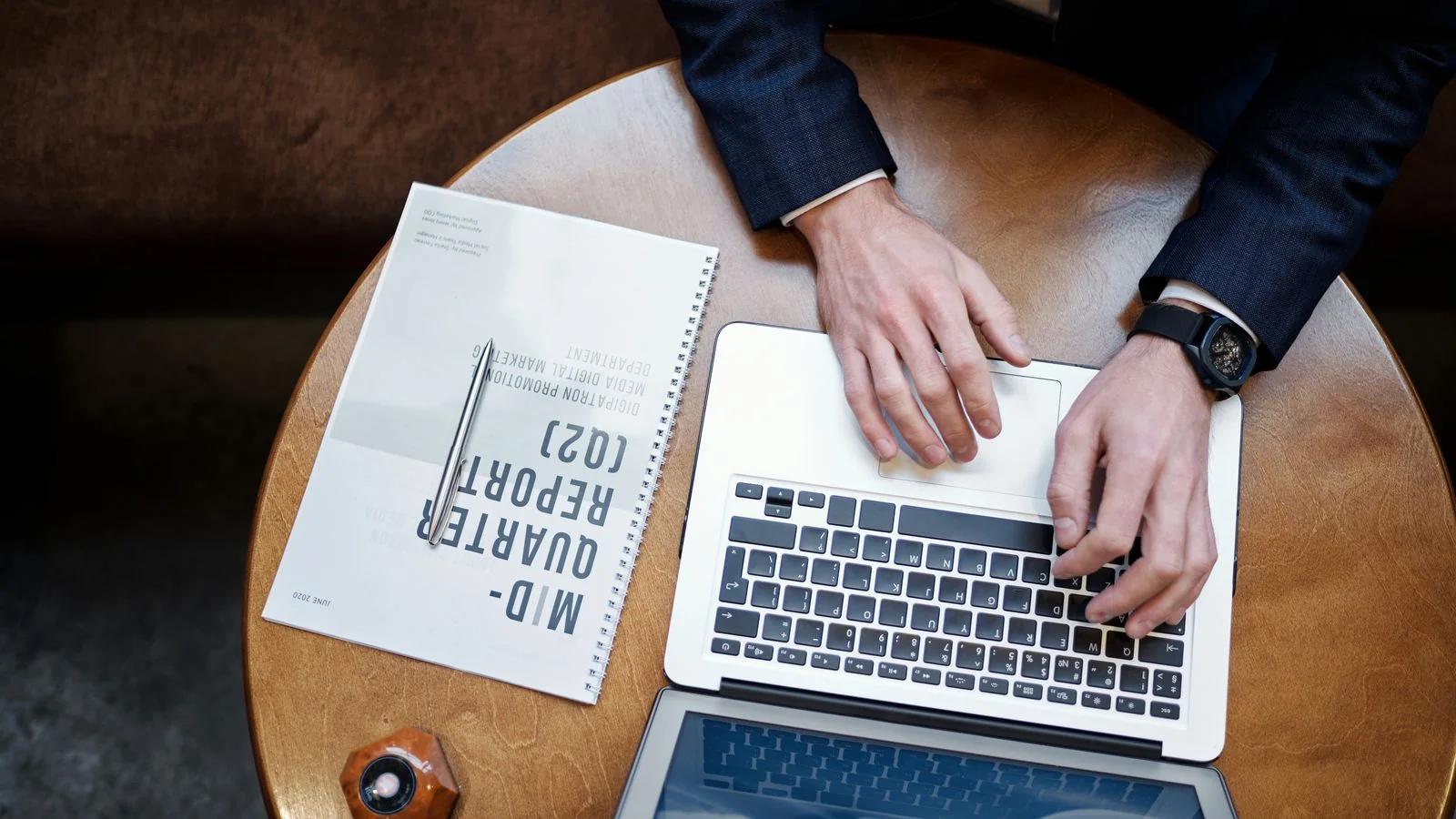 Businessman typing on a laptop beside a printed quarterly report, the monthly work behind a market brief people quote.