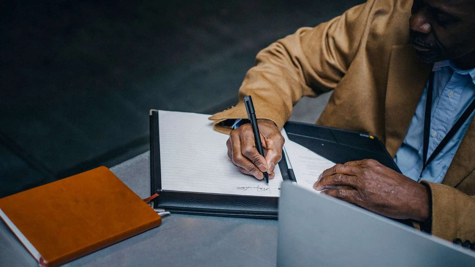An executive in a suit writing on paper beside a laptop and diary, weighing which vendor to trust