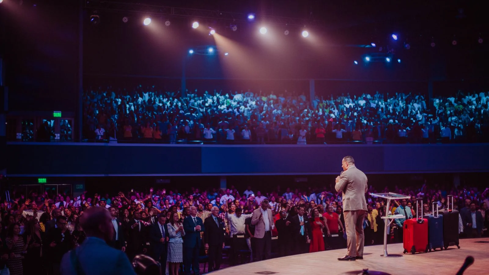 A speaker in a suit holding a large crowd on stage, authority made visible in a single room