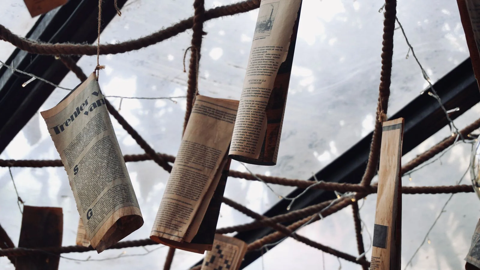 Vintage newspapers hanging from ropes across a ceiling, a reminder that press coverage is a key reference