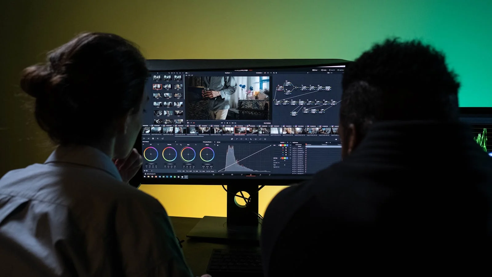 Two editors working with dual monitors on professional video editing software in a modern studio setup